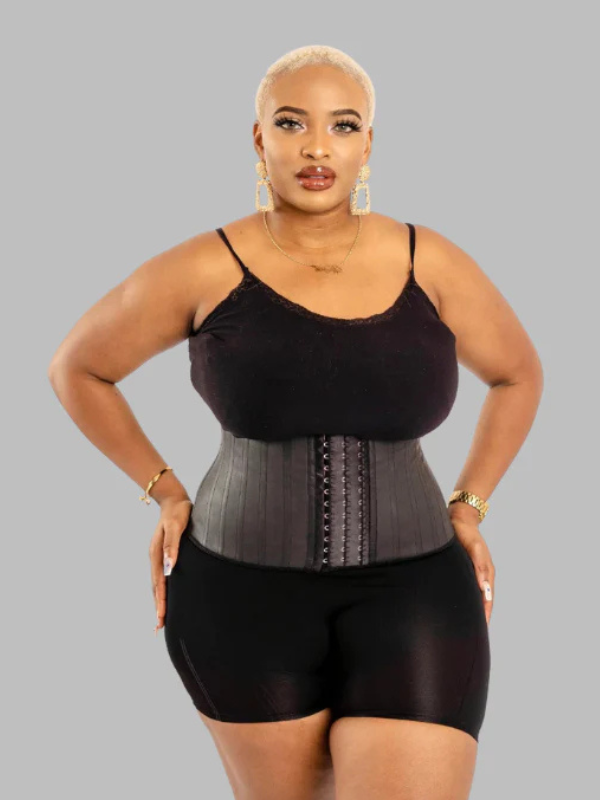 Model wearing black latex waist trainer shapewear with spiral steel boning and adjustable hook-and-eye closure.