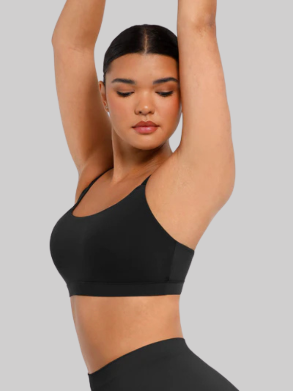 Woman stretching in a wireless black square neck bra with wide straps, showcasing comfort, flexibility, and a sleek seamless design.