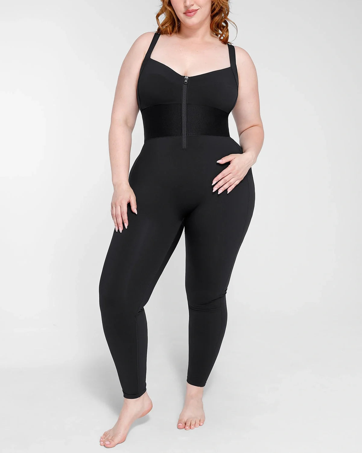 Full-body black waistband shaping jumpsuit with zipper front and adjustable shoulder straps, worn by plus-size model.